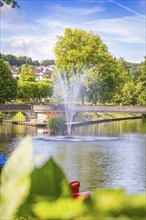 A fountain in the park, surrounded by green trees and a clear blue sky, Nagold, Black Forest,