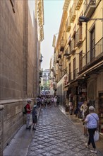 People stroll through a narrow street with shops in the old town, Granada