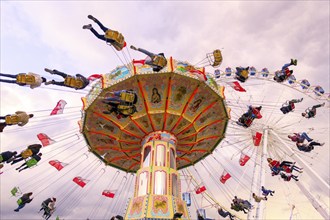 Chain carousel in motion with cheerful people in front of a cloudy sky, Ferris wheel, wave flight,