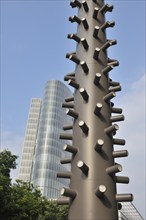 Modern sculpture with protruding metallic elements in front of a shiny skyscraper under a clear