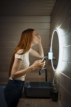 Young woman cleaning her face in washroom in the evening