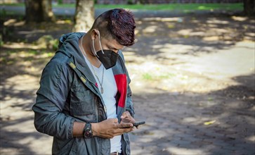 Man with a mask texting with his phone, young man with a mask texting with his cell phone, close up