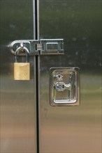 Close-up of stainless steel door on a utility cabinet locked with a brass padlock, Quebec, Canada,