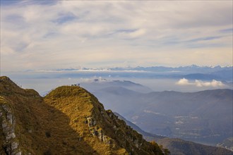 Aerial View over a Beautiful Mountainscape and a Mountain Peak with People and with Floating Clouds