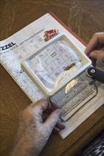 Elderly woman suffering from presbyopia, myopia, short-sightedness looking at crossword puzzle