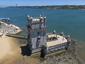 A historic tower on a rocky shore with blue water and sky in the background, aerial view, Torre de