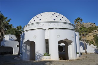 Round white building with domed roof and Mediterranean architecture surrounded by palm trees under