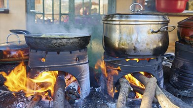 Several pots and pans cooking on open fires in a rustic kitchen, flames flickering on the logs,