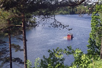 A tranquil scene by a lake with a red cabin in the water surrounded by dense green trees in the