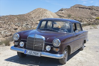 Brown Mercedes-Benz W110 classic car in the desert with sand and blue sky in the background, shiny