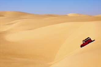 Off-road vehicle driving through vast sand dunes under a clear sky in a dry and sunny desert