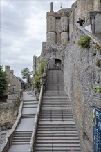 Stone steps lead upwards along a historic castle wall, under a cloudy sky, Le Mont-Saint-Michel