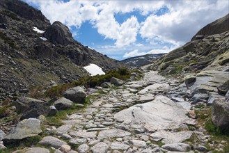 A stony path winds its way through a rocky mountain landscape under a cloudy sky, hiking area,