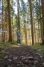 A woman stands on a forest path surrounded by tall trees, Unterhaugstett, Black Forest, Germany,