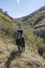 Traditional Kyrgyz eagle hunter with eagle in the mountains, hunting on horseback, near Kysyl-Suu,