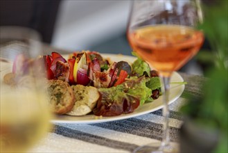 A plate of salad, bread and meat skewers, accompanied by a glass of rosé wine, ready to eat