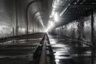 Dark tunnel with wet concrete walls and light at the end, industrial atmosphere, Rappbodetalsperre,