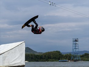 Man jumping with wakeboard over obstacle, somersault, water sports, water skiing and wakepark,