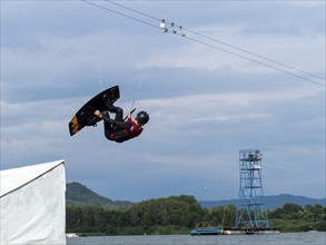 Man jumping with wakeboard over obstacle, somersault, water sports, water skiing and wakepark,