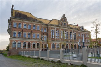 Imposing building with brick walls, large windows and fenced-in courtyard, St. Augustin Grammar