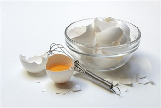 Egg shells in a glass bowl, whisk and opened hen's egg