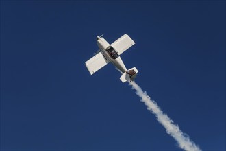 Stunt aerobatic plane performing stunts in blue sky with smoke trail. Concept of speed, difficulty,