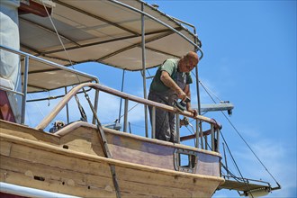 A man renovates a wooden boat in the dry dock on a sunny day, Patmos Marine, boatyard, Diakofti,