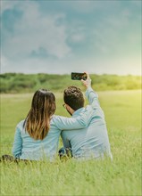 Young happy couple taking a selfie sitting in the field. Couple in love taking a selfie sitting in