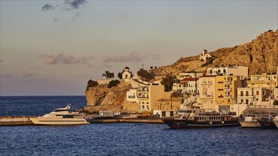 Boats moored in the harbour of a coastal town with churches and buildings on a rocky background,