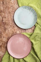 Two empty blue and pink plates on brown concrete background and green textile. Top view, close up,