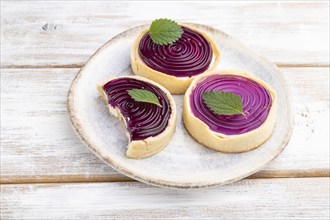 Sweet tartlets with jelly and milk cream on a white wooden background. Side view, close up