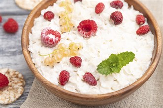 Rice flakes porridge with milk and strawberry in wooden bowl on gray wooden background and linen