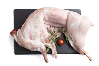 Whole raw rabbit with tomatoes, pea sprouts on a black concrete slate board isolated on white