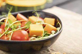 Vegetarian vegetable salad of tomatoes, pumpkin, microgreen pea sprouts on black concrete