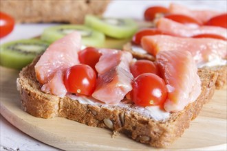 Smoked salmon sandwiches with butter and cherry tomatoes on white wooden background. close up