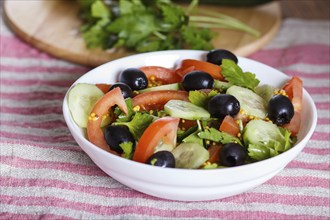 Vegetarian salad of tomatoes, cucumbers, parsley, olives and mustard on linen tablecloth, close up,