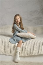 A serene image of a girl wearing a mint dress, sitting on a knitted blanket with a pillow. The soft