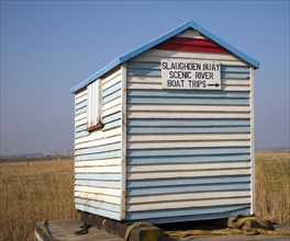 Old seaside beach hut with notice sign for boat trips at Slaughden, Aldeburgh, Suffolk, England,