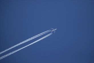 Boeing 747 aircraft flying across a blue sky leaving a contrail or vapor trail in the atmosphere