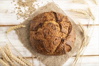 Fresh homemade golden grain bread with ears of wheat and rye on white wooden background and linen