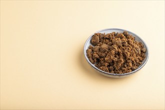 Plate with unrefined brown cane sugar on orange pastel background. side view, copy space