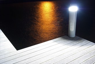 Pier with illuminated lamp and light reflections in the water at night, artistic, harbour village