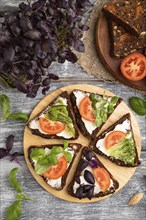 Grain rye bread sandwiches with cream cheese, tomatoes and basil microgreen on gray wooden