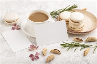 White business card mockup with cup of coffee, almonds and macaroons on gray concrete background.