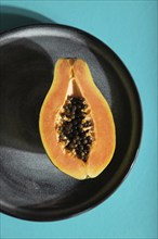 Ripe cut papaya on gray plate on blue pastel background. Top view, flat lay, close up, hard light.