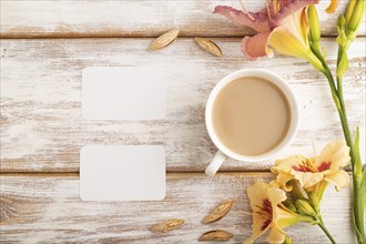 White paper business card mockup with orange day-lily flower and cup of coffee on white wooden