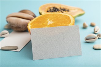 White paper business card with ripe cut papaya, orange, seashells on blue pastel pastel background.