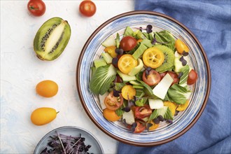 Vegetarian salad of pac choi cabbage, kiwi, tomatoes, kumquat, microgreen sprouts on a white