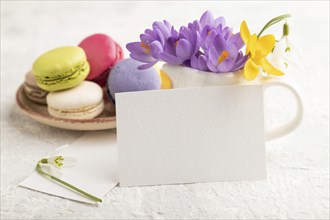 White paper business card mockup with spring snowdrop crocus flowers and multicolored macaroons on