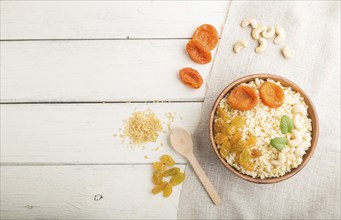 Bulgur porridge with dried apricots, raisins and cashew in wooden bowl on a white wooden background